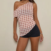 Woman wearing a one-shoulder plaid top and black shorts against a plain background